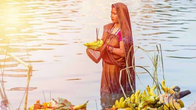 Women devotee offering Prasad to Sun God while standing in water during Chath Puja