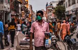 A man in shirt wearing a mask selling things on the street at Dashashwamedh road in Varanasi and people around the world and Kolkata exploring the city of Varanasi