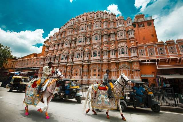 man in white and green long sleeve shirt standing near brown concrete building called the Hawa Mahal during daytime